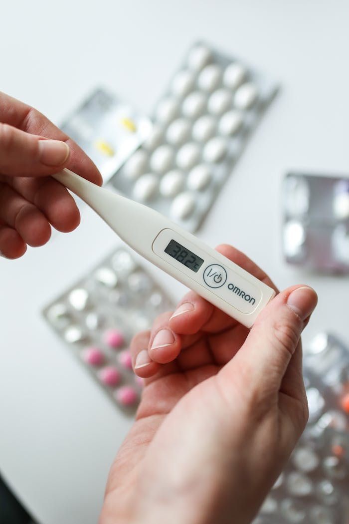 Close-up of hands holding a digital thermometer with medication in the background.